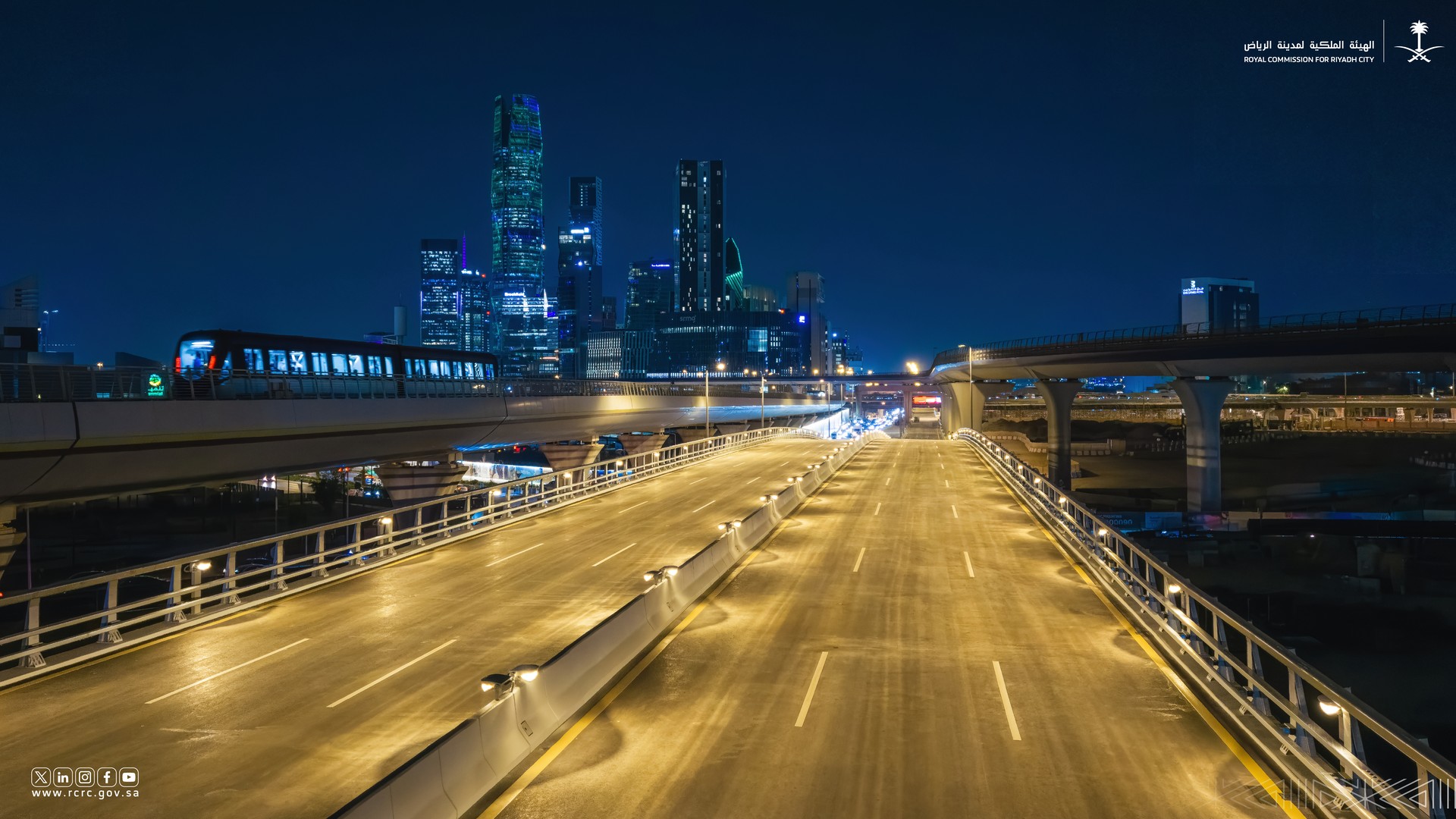 Al-Thumamah Road Bridge lit at night alongside the Riyadh Metro line, with King Abdullah Financial District towers behind