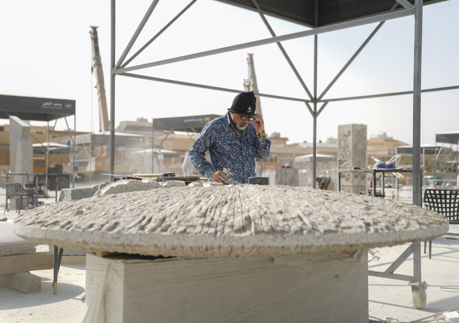A sculptor working on a large circular stone sculpture at the Tuwaiq Sculpture site