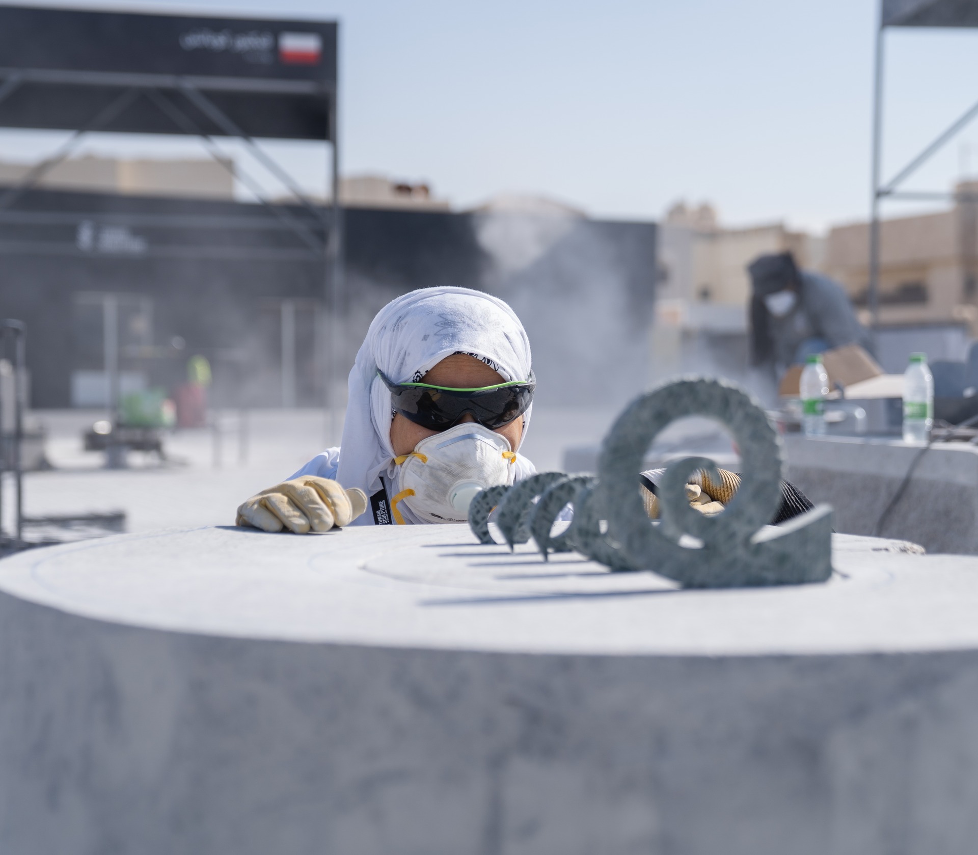 An artist carving a spiral-shaped stone work during Tuwaiq Sculpture