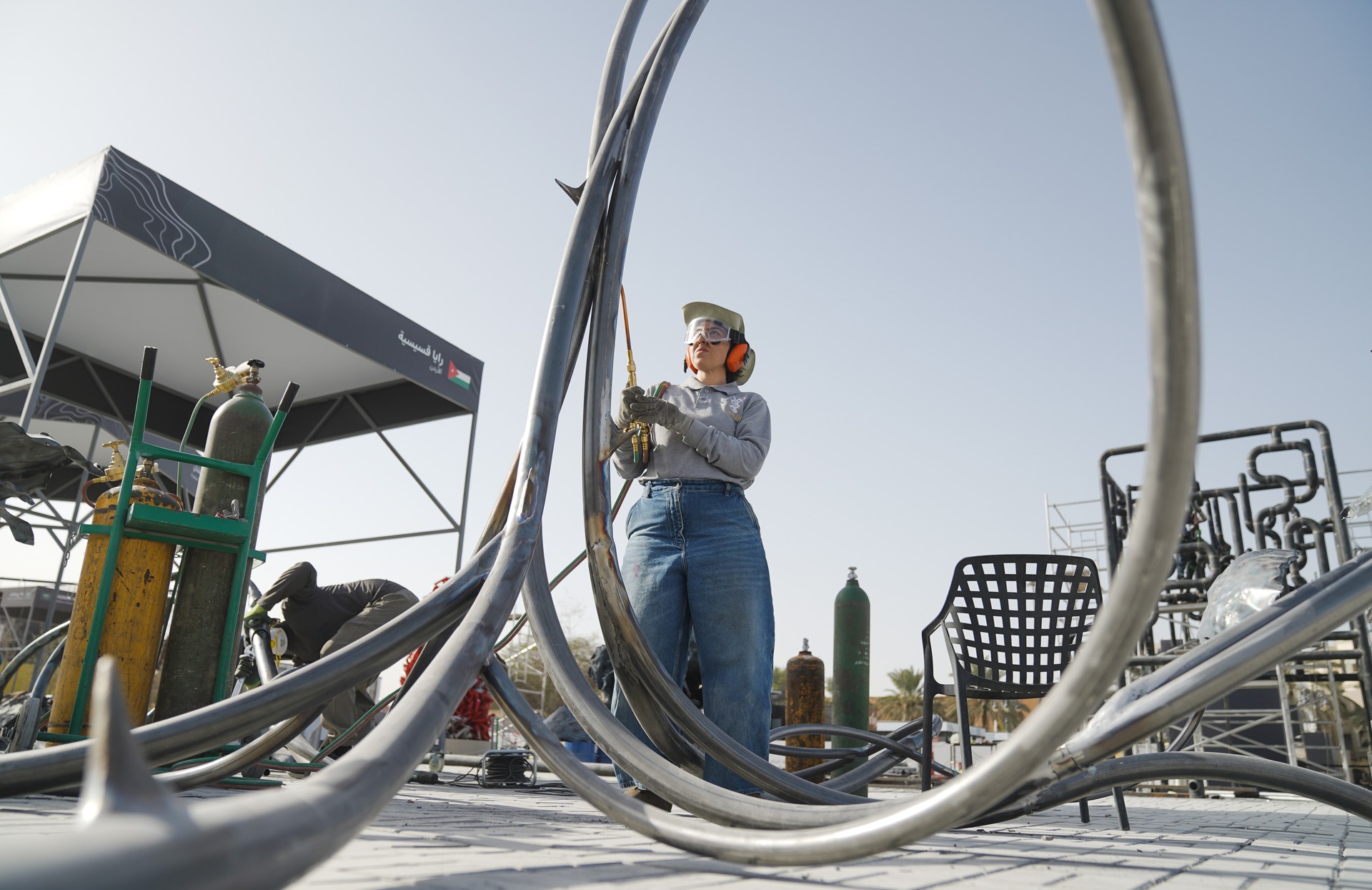 An artist welding curved metal tubes for a sculpture at Tuwaiq Sculpture